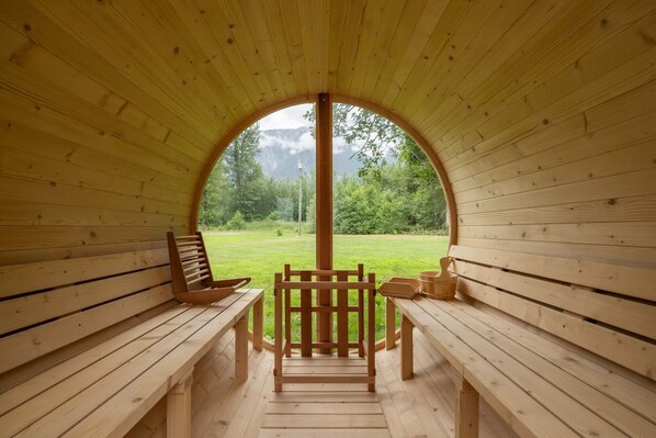 A wooden cabin with a semi-circular roof and a large arched window. Inside, there are wooden benches and a table.