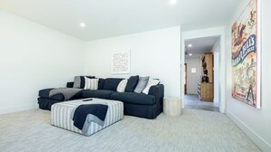 Een woonkamer met een modulaire bank, een gestreept voetenbankje en een poster aan de muur.