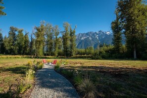 A gravel path leading to a seating area with chairs, surrounded by trees and a mountain backdrop. - Secluded house in Pemberton | Mount Currie Views | Sauna (Whistler)
