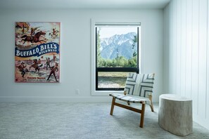 A room with a large window, a poster, a chair, and a round table. - Secluded house in Pemberton | Mount Currie Views | Sauna (Whistler)