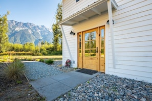 A white house with a wooden front door, a small porch, and a gravel driveway.