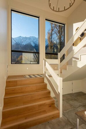 A staircase with wooden steps leading to a landing, large windows with a mountain view, and a modern chandelier.