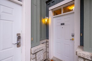 A house entrance with a stone base, a white door with a keypad lock, and a number plate '312' on the door. - Central location spacious 2 BDR | BBQ | Pet friendly | Free parking (Whistler)