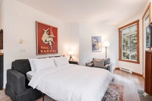 A bedroom with a bed, a chair, a lamp, a window, and a poster on the wall. - Central location spacious 2 BDR | BBQ | Pet friendly | Free parking (Whistler)