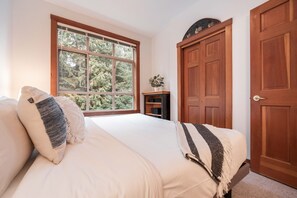A bedroom with a large window, a bed with pillows, a nightstand, and a wooden door. - Central location spacious 2 BDR | BBQ | Pet friendly | Free parking (Whistler)