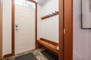 A hallway with a white door, a wooden bench, a coat rack, and a small rug. - Central location spacious 2 BDR | BBQ | Pet friendly | Free parking (Whistler)