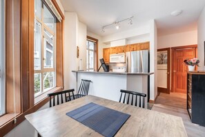 A modern kitchen with wooden cabinets, stainless steel appliances, and a dining area with a table and chairs. - Central location spacious 2 BDR | BBQ | Pet friendly | Free parking (Whistler)