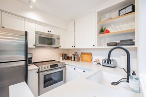 A modern kitchen with stainless steel appliances, white cabinetry, and a built-in oven. - Gorgeous 2+Loft | Creekside | Free Parking (Whistler)
