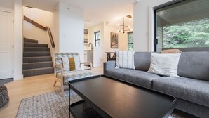 Ein modernes Wohnzimmer mit einem grauen Sofa, einem gemusterten Sessel, einem schwarzen Couchtisch und einer Treppe, die in einen Küchenbereich führt.