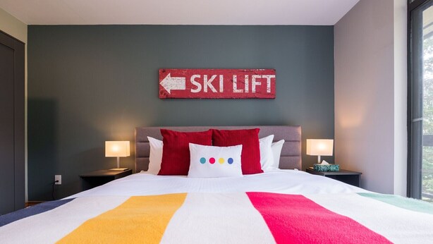 Une chambre d’hôtel avec un lit, deux tables de chevet, un panneau fixé au mur et une fenêtre.