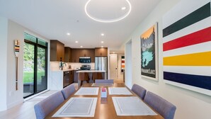 Une cuisine moderne dotée d’un îlot central, d’un coin repas avec une longue table et des chaises, et d’une grande fenêtre offrant une vue sur l’extérieur.
