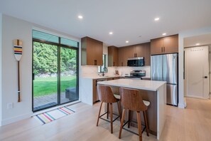 A modern kitchen with a large island, wooden cabinets, stainless steel appliances, and a sliding glass door to the outdoors.