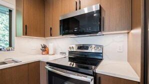 Une cuisine moderne avec des meubles en bois, un four à micro-ondes en acier inoxydable, un four et un plan de travail agrémenté d’un bloc à couteaux et d’un rouleau d’essuie-tout.