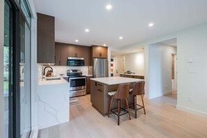 Een moderne keuken met inbouwapparatuur, een centraal eiland en houten barstoelen.
