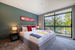 A modern bedroom with a large bed, two bedside tables, a "SKI LIFT" sign, and a large window offering a view of trees and mountains.