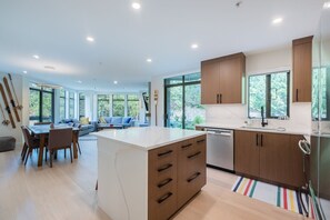 Eine moderne Küche mit Holzschränken, einer zentralen Kochinsel und einem Essbereich mit einer Couch und einem Tisch.