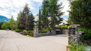 A residential area with a stone entrance gate, a paved driveway, and a mountain backdrop. - Private Hot Tub | Pets | Free Parking | Location! (Whistler)