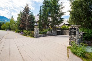 A residential area with a stone entrance gate, a paved driveway, and a mountain backdrop. - Private Hot Tub | Pets | Free Parking | Location! (Whistler)