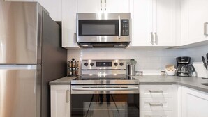 A modern kitchen with stainless steel appliances, white cabinetry, and a coffee maker. - Private Hot Tub | Pets | Free Parking | Location! (Whistler)