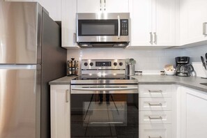A modern kitchen with stainless steel appliances, white cabinetry, and a coffee maker. - Private Hot Tub | Pets | Free Parking | Location! (Whistler)