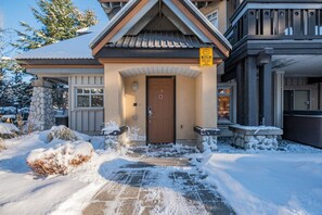 A two-story building with a stone facade, a wooden door, and a caution sign about snow slides. - Private Hot Tub | Pets | Free Parking | Location! (Whistler)