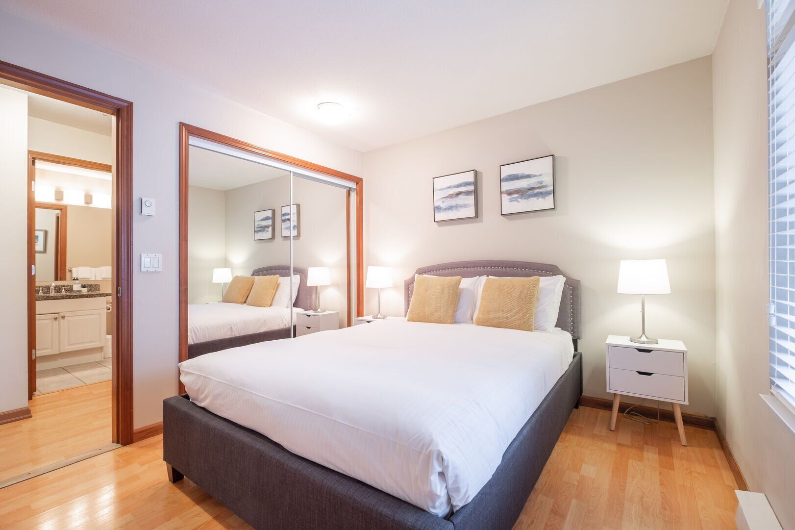 A hotel room with a large bed, bedside tables, a mirror, and artwork on the wall.