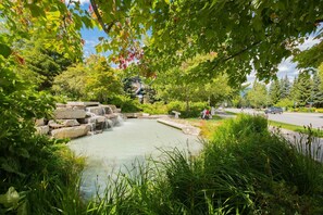A natural water feature with a stone waterfall, surrounded by lush greenery and a clear sky. - Private Hot Tub | Pets | Free Parking | Location! (Whistler)