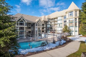 A multi-story hotel with a central courtyard featuring a swimming pool, surrounded by snow and trees. - Stunning views | Ski-in/out | Pool | Hot Tub | BBQ (Whistler)