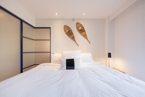 A hotel room with a bed, white bedding, a black pillow, a wall-mounted light, and two wall decorations. - Stunning views | Ski-in/out | Pool | Hot Tub | BBQ (Whistler)