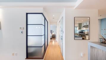 Ein modernes Interieur mit einem Flur, der zu einer Küchenecke führt, mit einer Glastrennwand, einem Wandspiegel und Holzboden.