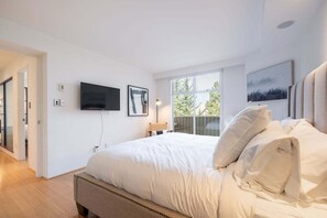 Ein Schlafzimmer mit einem großen Bett, einem an der Wand montierten Fernseher und einem Fenster mit Blick auf Bäume.