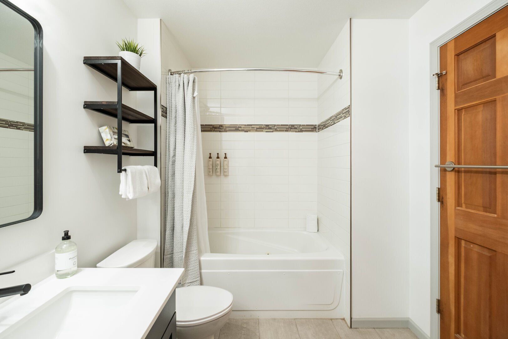 A bathroom with a white toilet, a bathtub, a shower curtain, and a wooden door.