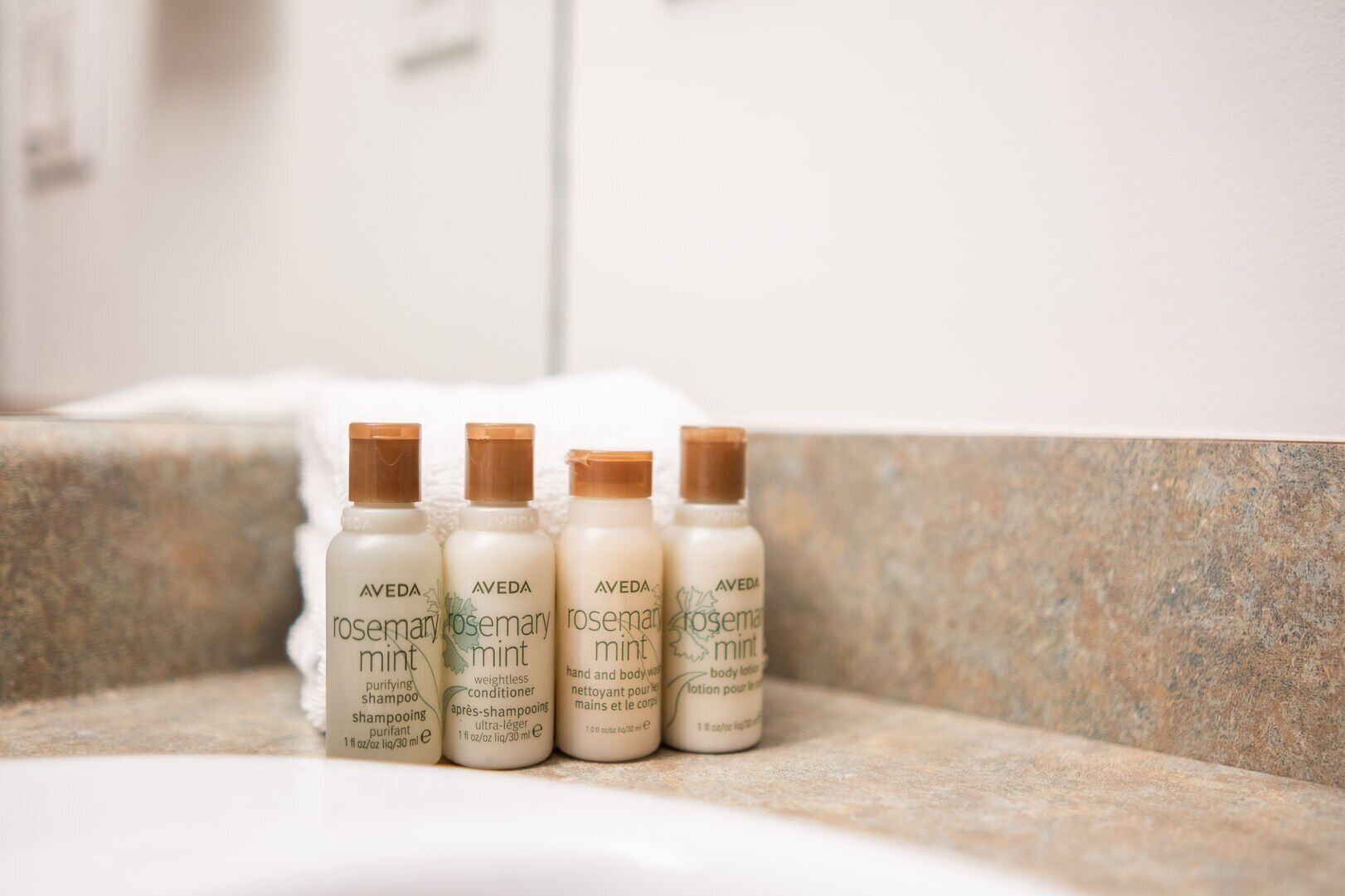 Cuatro botellas de loción corporal romero y menta de Aveda sobre una encimera de baño.