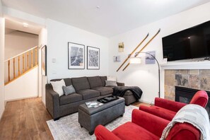 A living room with a grey sofa, red armchairs, a fireplace, and a TV mounted above it. - Perfect location | Free Parking | Pool & Hot Tub (Whistler)