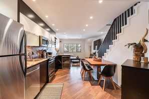 Une cuisine moderne dotée d’un réfrigérateur en acier inoxydable, d’un plancher en bois et d’un coin repas avec une table et des chaises.