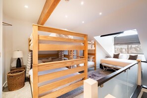 Ein modernes Schlafzimmer mit Etagenbett, einer Schlafcouch, einer Lampe und Blick auf eine verschneite Landschaft durch ein großes Fenster.