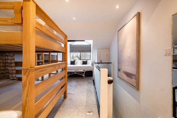 Une chambre avec un lit superposé, une table de chevet, une fenêtre donnant sur un beau paysage et un tableau accroché au mur.