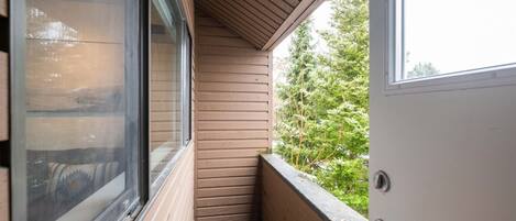 Un balcon en bois avec une fenêtre, une porte et une vue sur les arbres.