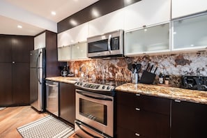 A modern kitchen with stainless steel appliances, a granite countertop, and dark cabinetry. - Spacious Rustic 1BDR in the Heart of Whistler (Whistler)