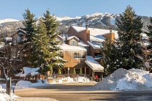 Eine Berghütte mit verschneitem Dach, Holzfassade und Blick auf schneebedeckte Berge.