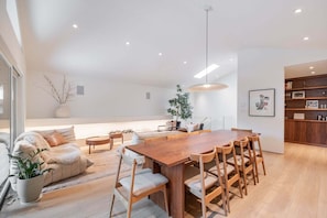 Ein modernes Interieur mit einem Holztisch, Stühlen, einer Couch und einer Pendelleuchte.