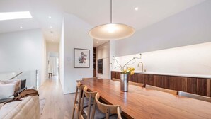 Een moderne keuken met een houten eettafel, stoelen, een hanglamp en een vaas met bloemen.