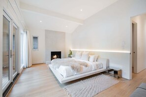 Ein modernes Schlafzimmer mit einem großen Bett, einem Kamin und einer Glastür, die auf einen Balkon führt.