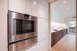 A modern kitchen with stainless steel appliances, a built-in oven, and a large window overlooking a snowy landscape. - Elegant Chalet | Walk to Blackcomb Gondola | Sauna and Cold plunge (Whistler)