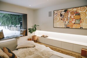 A modern bedroom with a large window, a sofa, a bed, a plant, and a wall-mounted artwork. - Elegant Chalet | Walk to Blackcomb Gondola | Sauna and Cold plunge (Whistler)