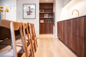 A modern kitchen with wooden cabinets, a wooden dining area, and a framed artwork on the wall. - Elegant Chalet | Walk to Blackcomb Gondola | Sauna and Cold plunge (Whistler)