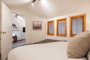 Ein Schlafzimmer mit einem Bett, einer Tür zu einem anderen Raum und drei Fenstern mit Holzrahmen.