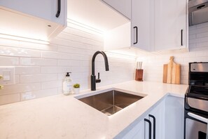 A modern kitchen with white cabinetry, a stainless steel sink, a black faucet, and a built-in oven. - 2+loft | Walk to Creekside Gondola | Pet friendly (Whistler)