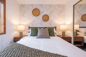 Uma cama bem arrumada com um cobertor texturizado, duas luminárias de mesa e um espelho na parede.