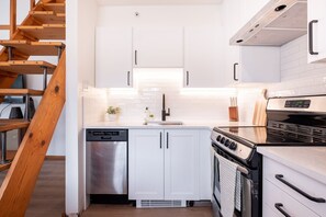 Eine moderne Küche mit weißen Schränken, einem Edelstahl-Geschirrspüler, einem Backofen und einer Holztreppe.
